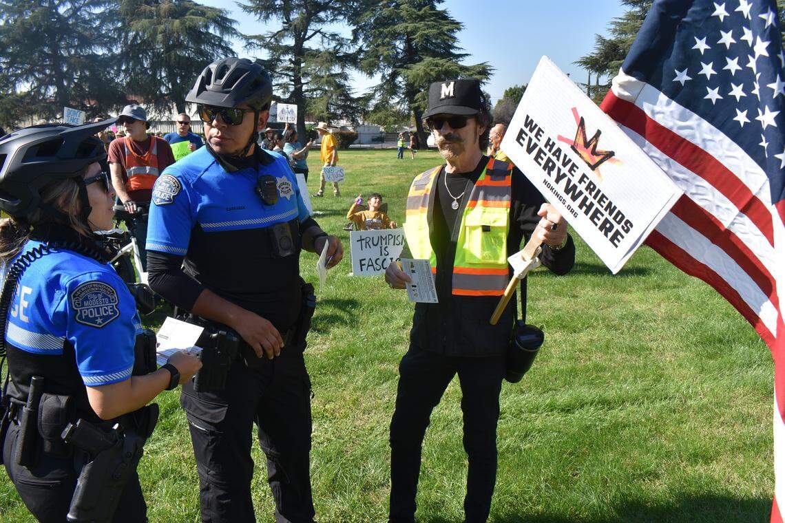 The second No Kings rally in Modesto this year was held in Standiford Park on Tokay Avenue in Modesto, Calif., on Saturday, Oct. 18, 2025. Police officers tell protester James Chavez Jr. that the diameter of the flagpole he is carrying exceeds that allowed under municipal code.