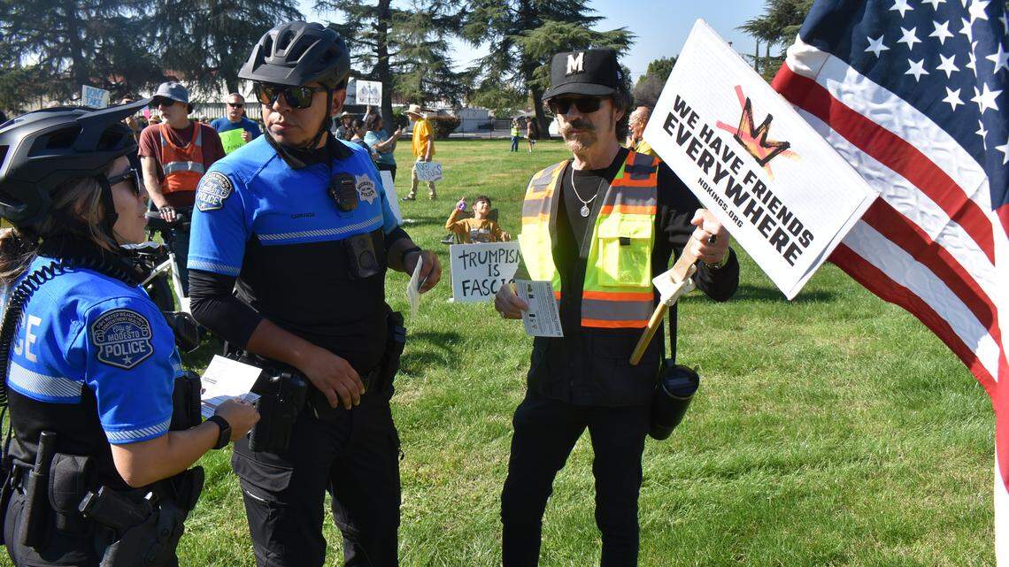 The second No Kings rally in Modesto this year was held in Standiford Park on Tokay Avenue in Modesto, Calif., on Saturday, Oct. 18, 2025. Police officers tell protester James Chavez Jr. that the diameter of the flagpole he is carrying exceeds that allowed under municipal code.
