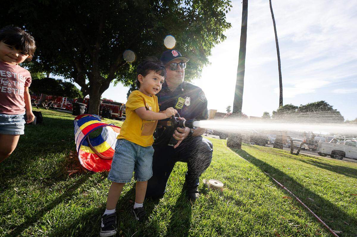 Julian Marrufo, 2, blasts a target with the help of Patterson firefighter Shane Eddington during National Night Out at North Park in Patterson, Calif., Tuesday, Aug. 1, 2023.