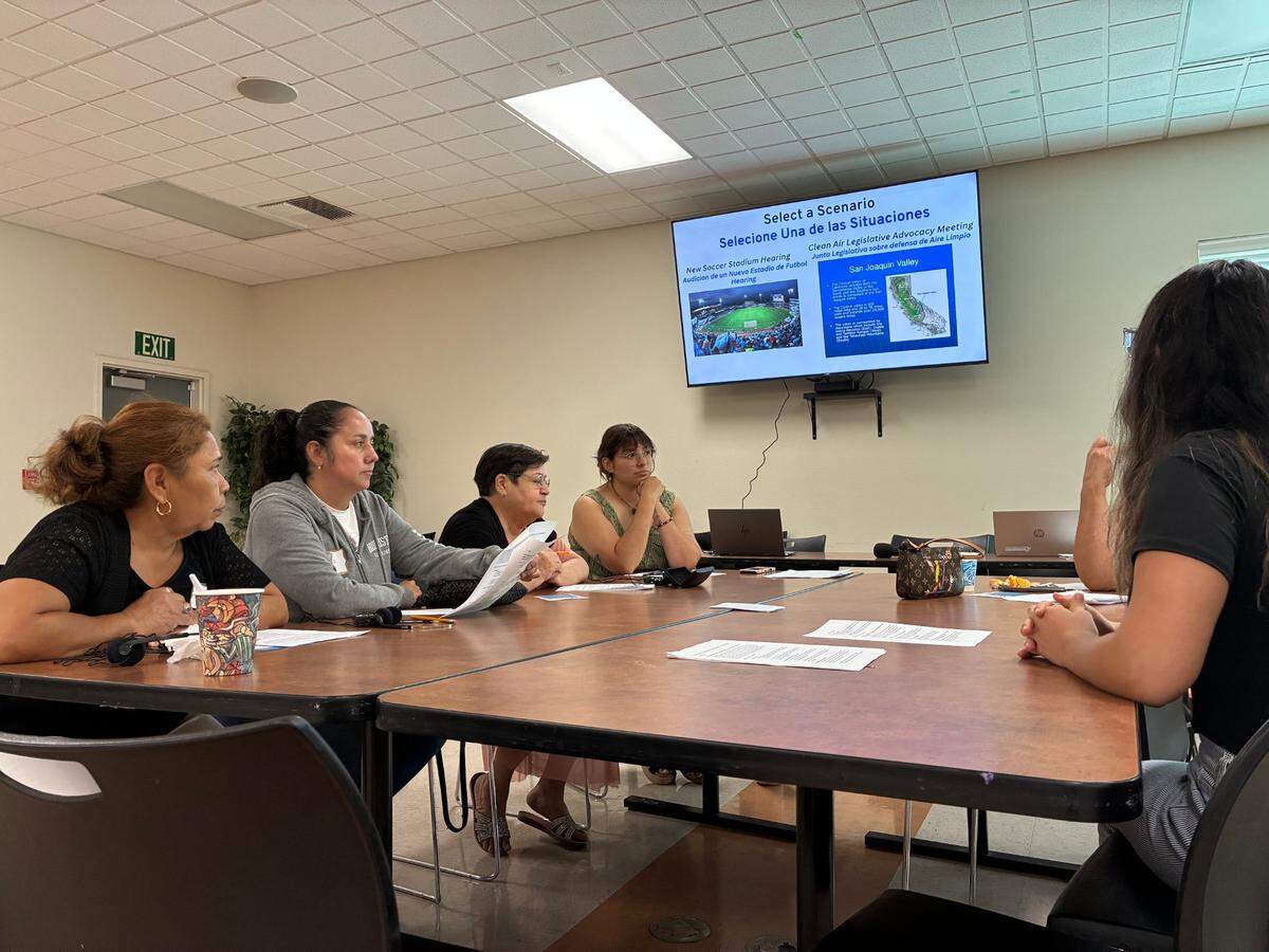 Women stand around a table reading out the instructions for a role-playing exercise on air quality issues in West Modesto. 