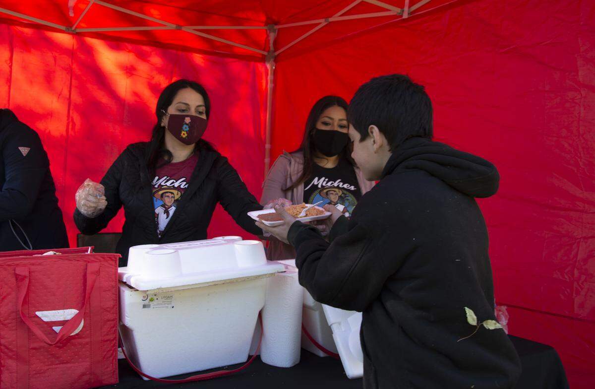 John Charles Harnden, 10, receives a plate of food from Lupe Velarde (left) and Enedina Rincon of Miches el Kora in Modesto on Thanksgiving Day 2020 in Graceada Park in Modesto, Calif.