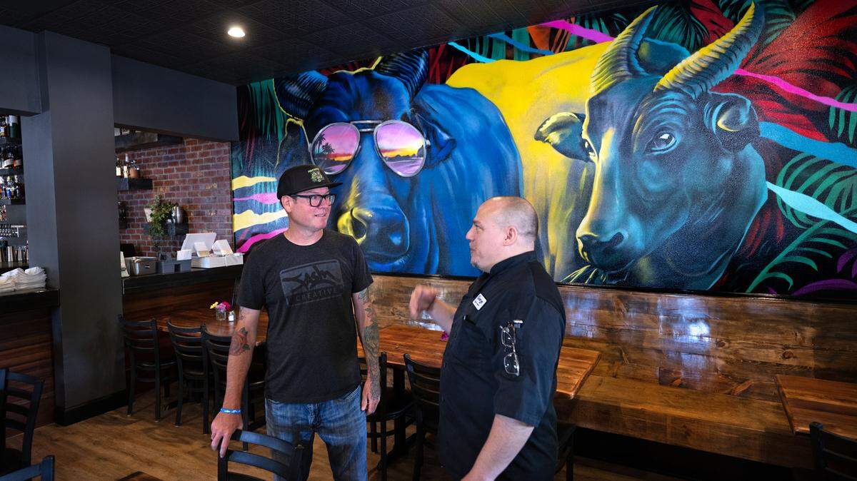 Artist FASM aka Aaron Vickery talks with owner George Bertaina, right, in Cora restaurant at Roseburg Square in Modesto, Calif., Friday, May 24, 2024. FASM painted the mural on the dining room wall.