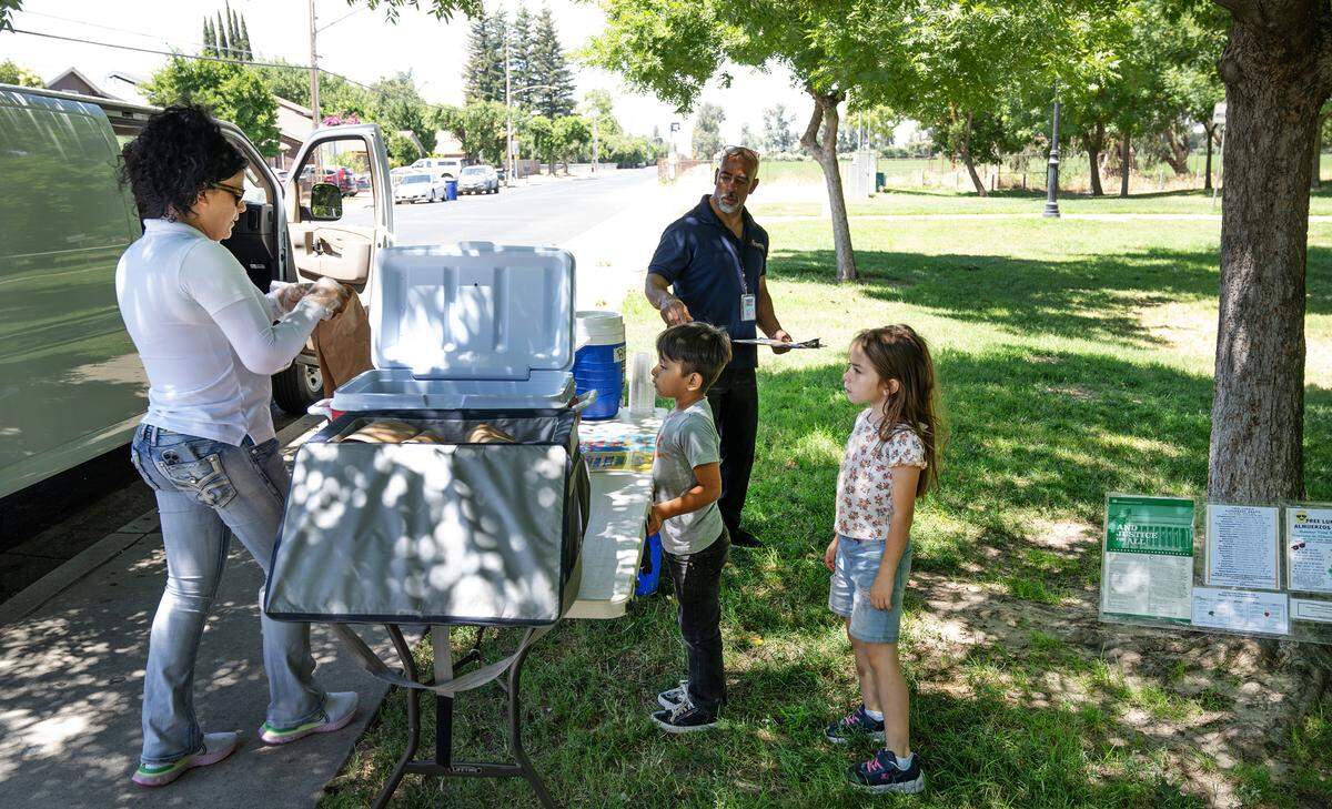 Nutrition services employee Lilianna Trujillo, left, serves up lunch to children during Modesto City Schools’ summer lunch program at Mark Twain Park on California Avenue in Modesto, Calif., Tuesday, June 25, 2024.
