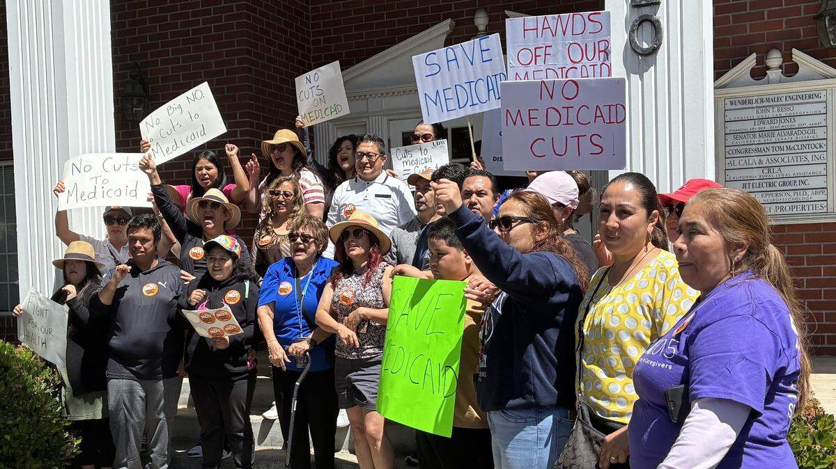 Approximately 50 people holding signs that read "Save MediCaid" and "Hands Off our Medicaid" are standing infront of the building's steps.
