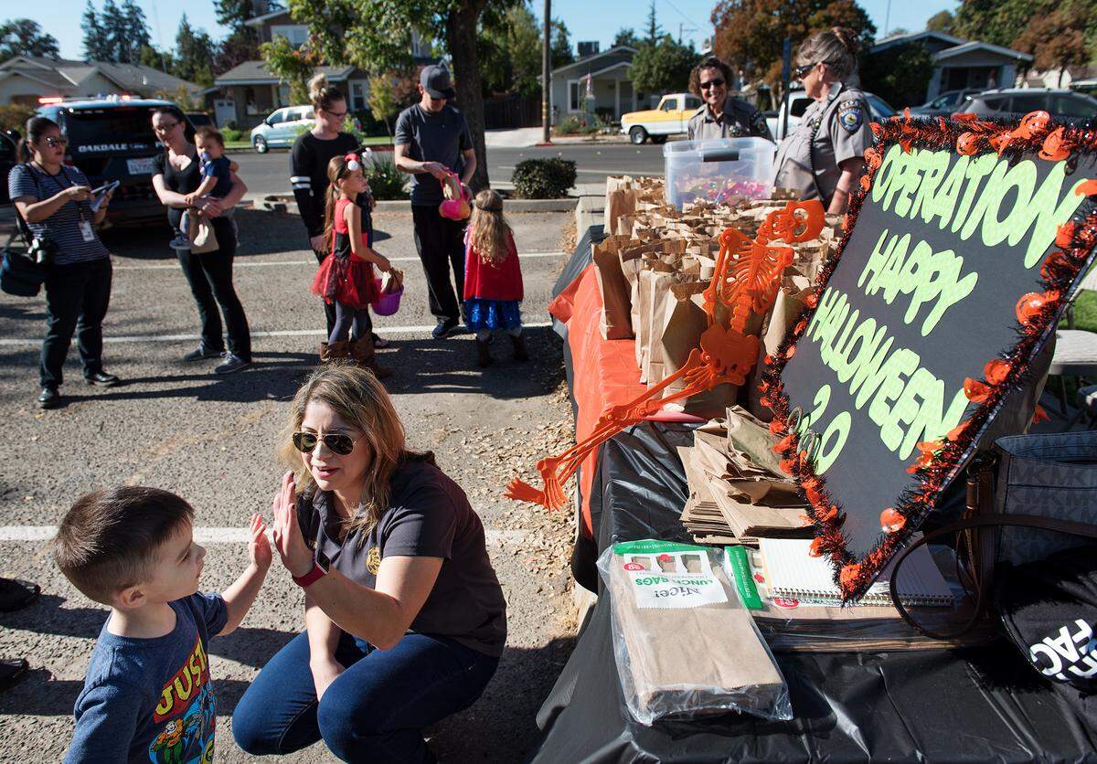 Oakdale Police Public Information Officer Janeen Yates gives gives a high-five to three-year-old Daniel Burket Jr.  during Operation Happy Halloween 2.0 in Oakdale, Calif., Saturday, Nov. 3, 2018. Oakdale Police gave away candy to children as a way to replace tainted candy that was found on Halloween day in the Burchell Hill Drive area.  