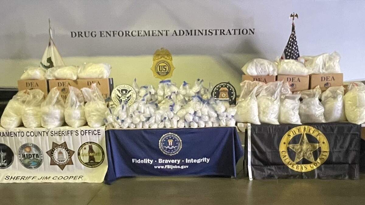 Bags of suspected methamphetamine and boxes labeled as evidence are displayed alongside law enforcement insignia during a multi-agency operation that authorities say resulted in the seizure of roughly 2,700 pounds of methamphetamine.