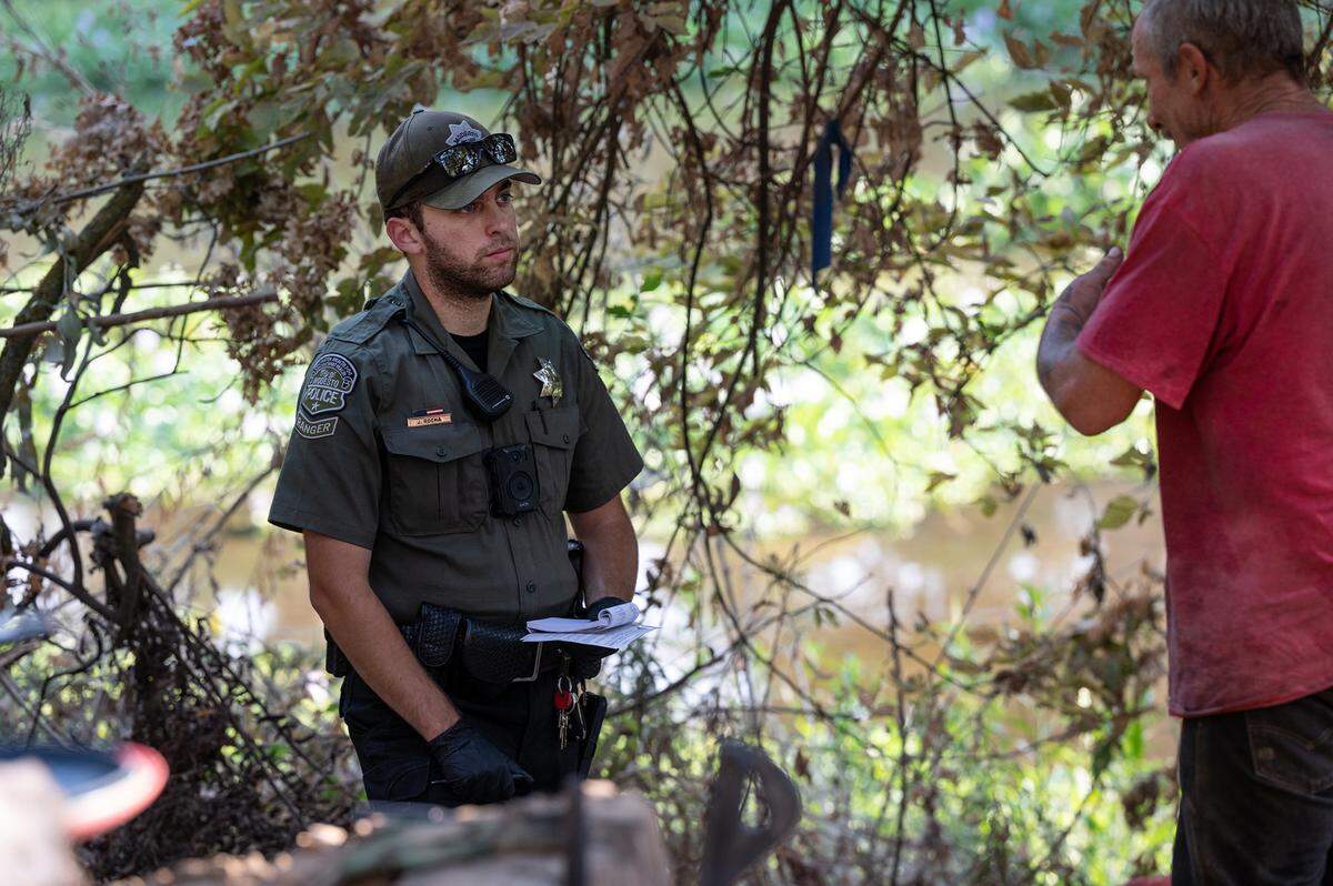 Modesto park ranger Justin Rocha talks with a homeless man about shelter services at a campsite along the Tuolumne River in Modesto, Calif., on Friday, September 9, 2022.