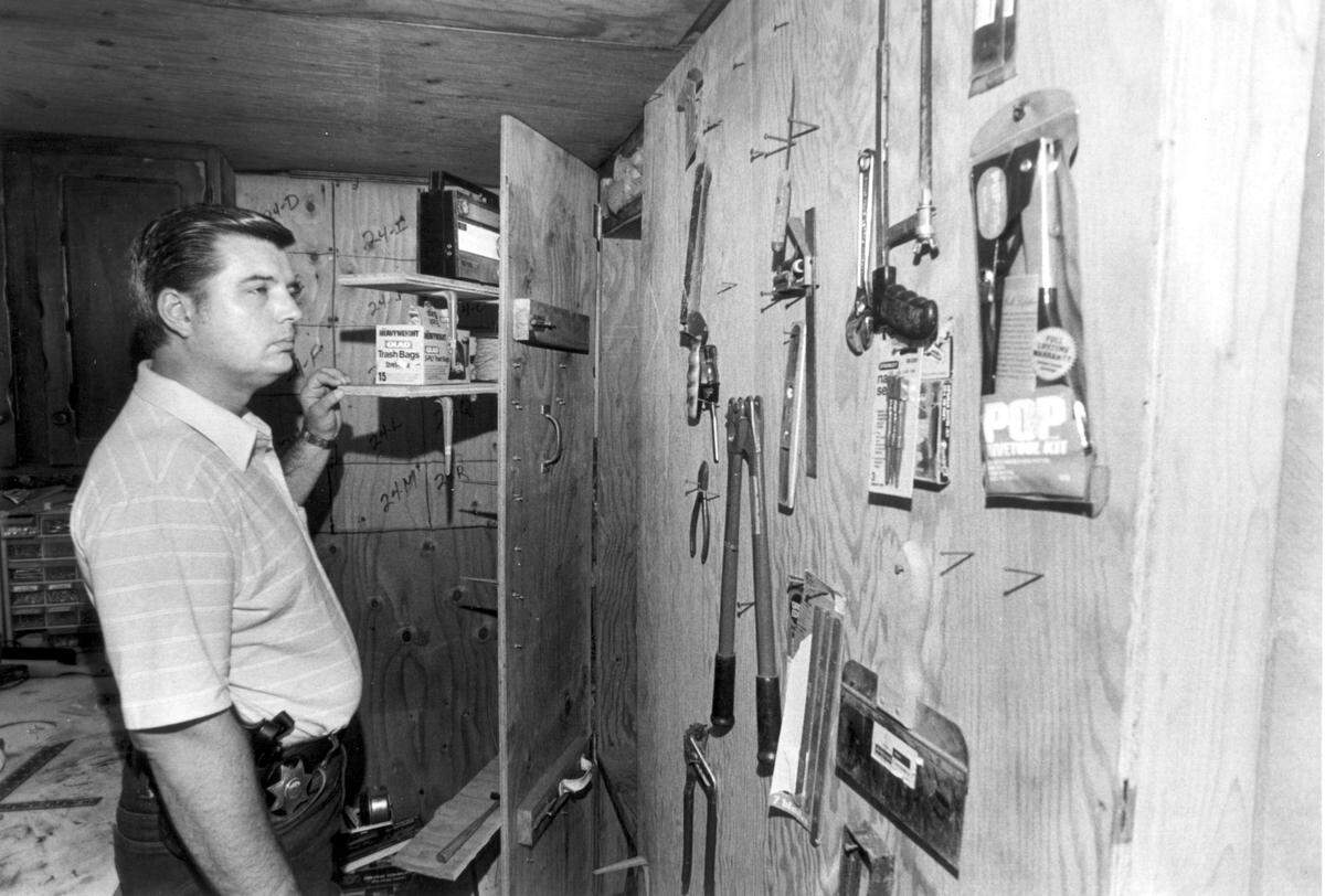Calaveras County spokesman Jim Stenquist shows on June 16, 1985, how an ordinary-looking wall with tool shelves mounted on it concealed the entrance to the secret bunker chamber where serial killers Charles Ng and Leonard Lake tortured and murdered their victims.