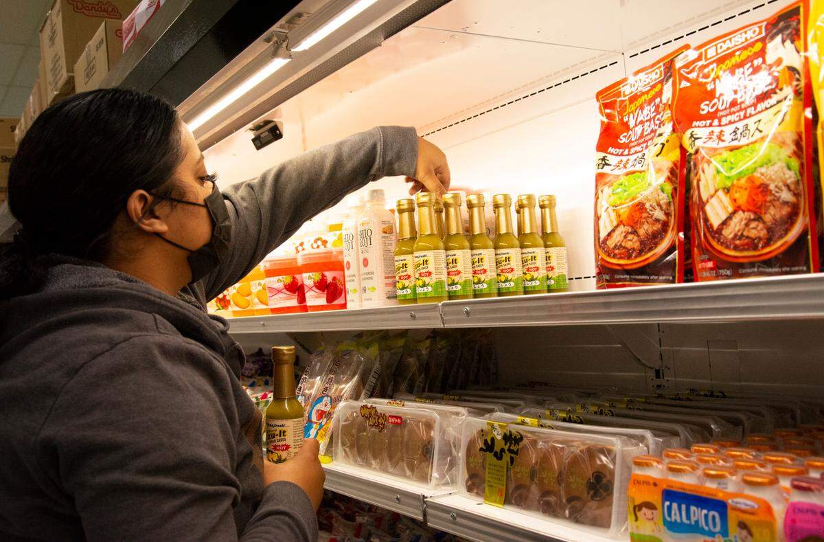 Asian Market employee Jayden Nglam stocks shelves in the specialty grocery store that is reopening after a fire.