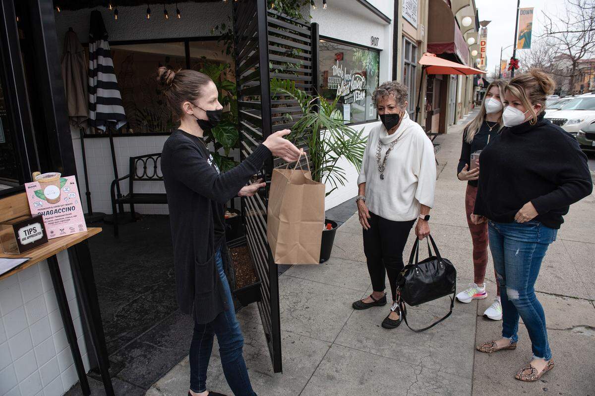 Farmacy restaurant manager Rachel Morrisette delivers take-out to Francesca Orr, right, her daughter Delaney and friend Shari Lloyd, left, in Modesto, Calif., on Thursday, Jan. 6, 2022. The restaurant closed to indoor dining due to the spike in COVID-19 cases.