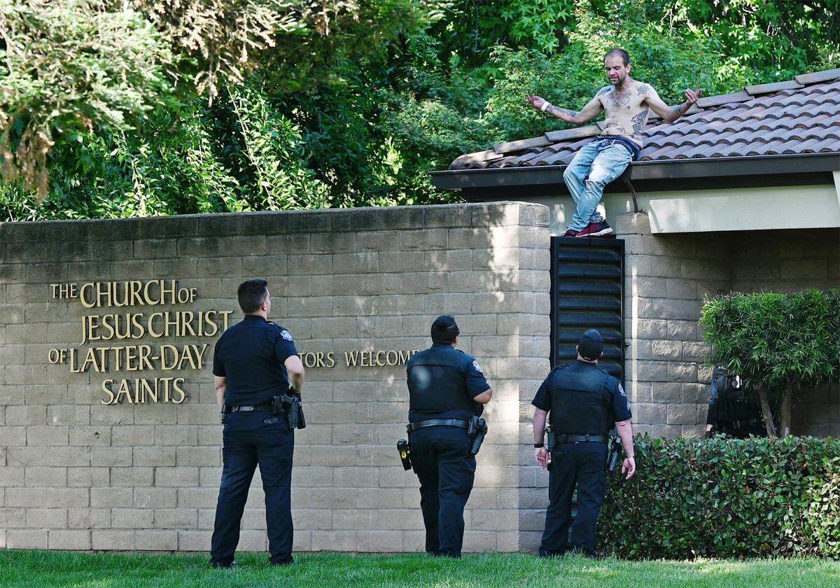 Modesto Police talk with a distraught man on the roof of the Church of Jesus Christ of Latter-Day Saints church on Dale Road in Modesto, Calif., on Tuesday, April 26, 2022. The man ripped up and destroyed dozens of tiles on the church roof.