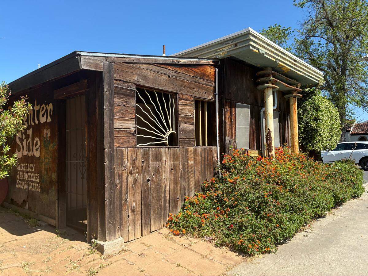 An old eclectic-looking wooden building with metal pillars in the front that houses a community gathering spot, a cash-only downtown sandwich shop.