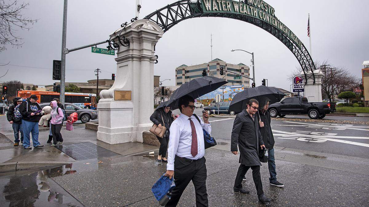 People walk down I Street during a rainstorm in Downtown Modesto, Calif., Thursday, Feb. 14, 2019.