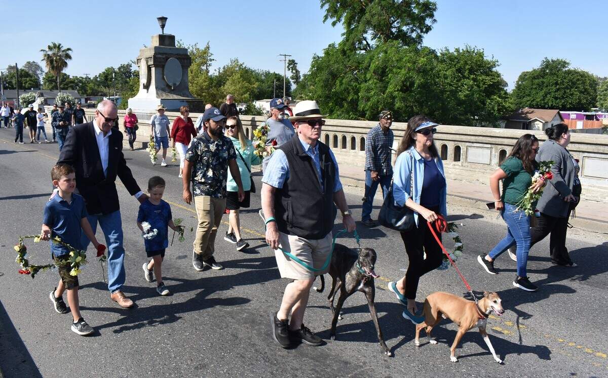 Attendees of a Memorial Day commemoration, including Stanislaus County Supervisor Terry Withrow, at left with his grandsons, carry flowers to toss into the Tuolumne River from the Seventh Street bridge Monday morning, May 29, 2023.