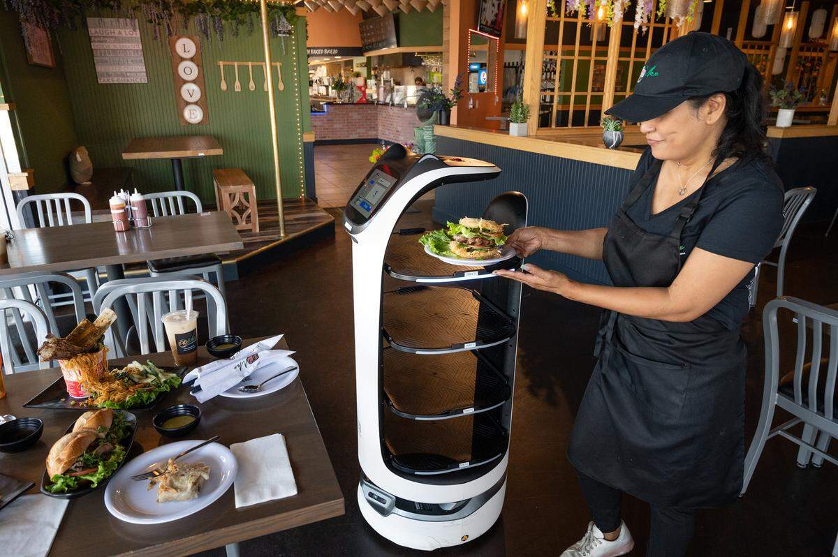Owner Tina Tien grabs a plate off the server robot at Pho Mex restaurant in Modesto, Calif., on Thursday, June, 23, 2022.