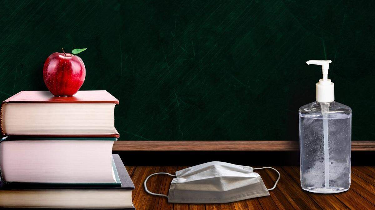 Back to school during Covid-19 pandemic with classroom setting of apple on books to signify education, and bottle of sanitizer and face mask on table. Concept of new school measures to contain coronavirus outbreak. Copy space on chalk board. (Back to