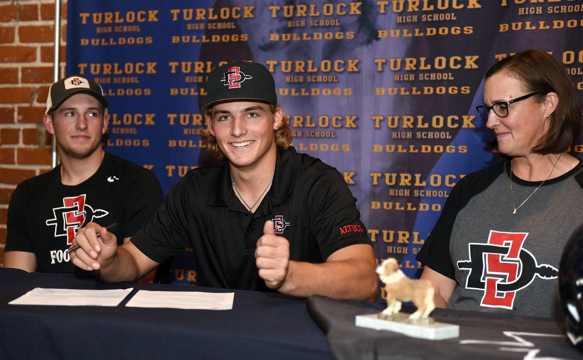 Turlock high school senior Garret Fountain (center) gives a thumbs up while he signs his letter of intent with San Diego State University on Friday December 21, 2018 at Red Brick Bar & Grill in Turlock, Calif. Also pictured are Garret’s older brother Walt (left) and mother Karen.