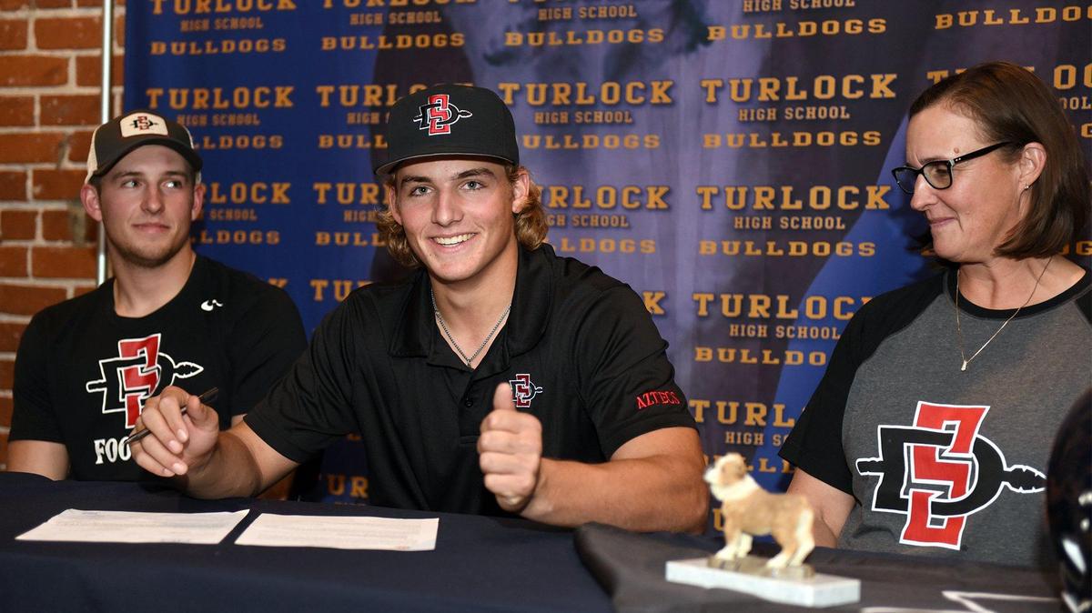 Turlock high school senior Garret Fountain (center) gives a thumbs up while he signs his letter of intent with San Diego State University on Friday December 21, 2018 at Red Brick Bar & Grill in Turlock, Calif. Also pictured are Garret’s older brother Walt (left) and mother Karen.