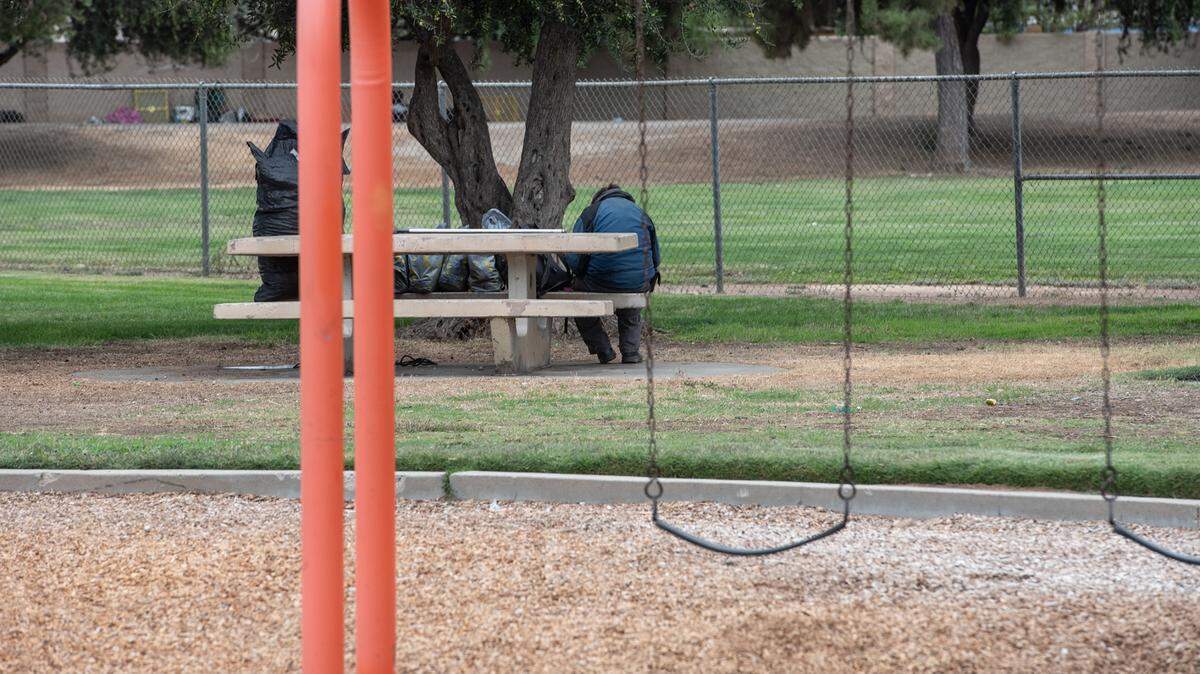 A homeless person sits on a park bench at Mellis Park in Modesto, Calif., on Wednesday, Oct. 20, 2021.