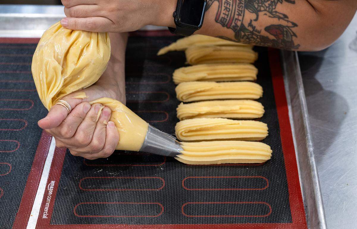 Baker Elizabeth Zavala squeezes out eclair forms at the Bakeshop in Modesto, Calif., Thursday, Oct. 12, 2023.