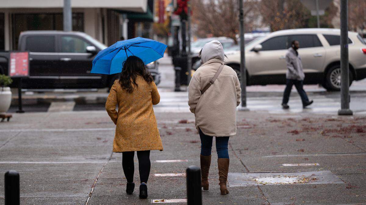 People walk down 10th Street in downtown Modesto, Calif., during a light rain Thursday, Dec. 1, 2022.