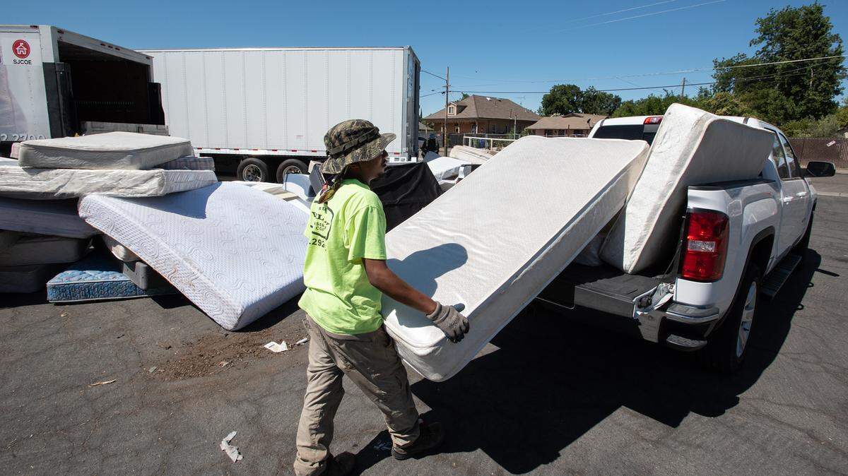 California Conservation Corp member Anthony Williams unloads mattresses during a Modesto city sponsored trash day at John Thurman Field in Modesto, Calif., on Saturday, June, 25, 2022. The mattresses and box springs are recycled by Bye Bye Mattress.