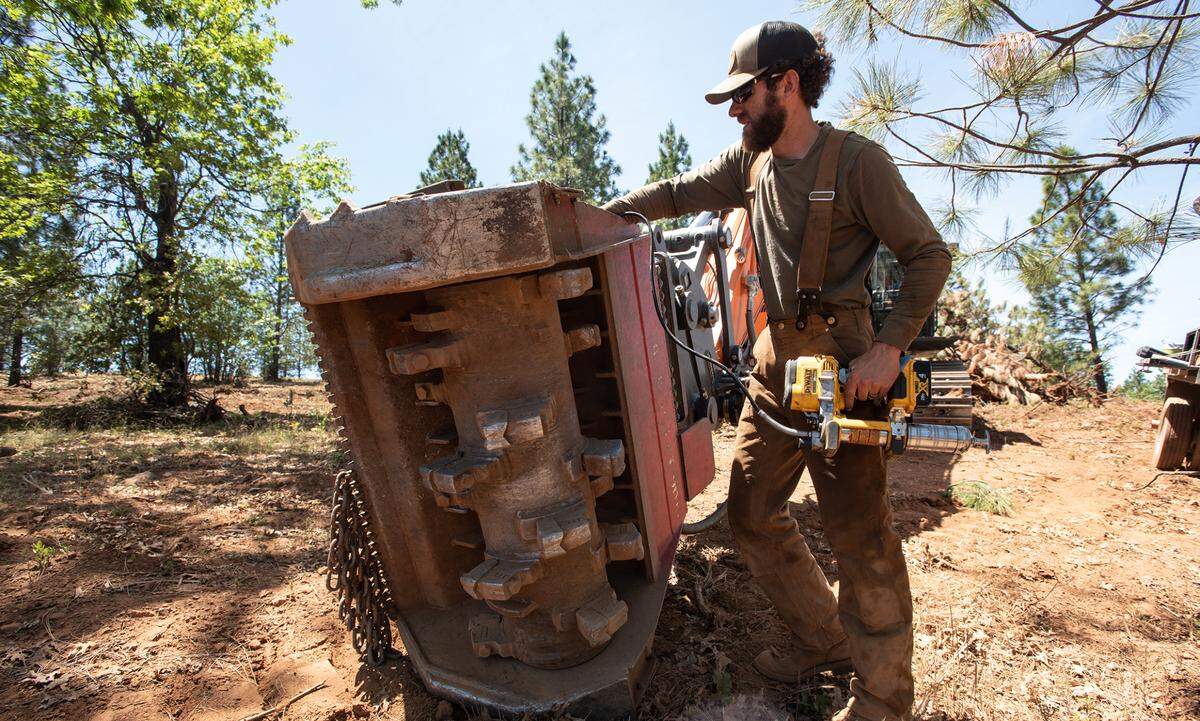 Contractor Wesley Brinegar finishes maintenance on a masticator after a day of working on a fuel break in the Stanislaus National Forest near Cedar Ridge, Calif., on Friday, May 20, 2022.