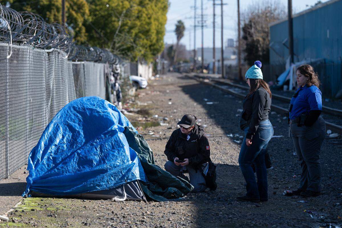 Community Health and Assistance Team (CHAT) outreach specialist Christina Kenney kneels down to survey a homeless man during Stanislaus County’s Point-in-Time count of unsheltered homeless people in Modesto, Calif., Thursday, Jan. 25, 2024. Community Health and Assistance Team (CHAT) outreach specialist Megan Dill, right, and BHRS housing specialist Asuzena Pena, middle, assist in the count.