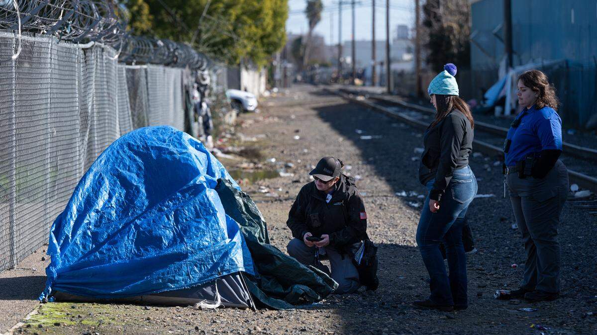 Community Health and Assistance Team (CHAT) outreach specialist Christina Kenney kneels down to survey a homeless man during Stanislaus County’s Point-in-Time count of unsheltered homeless people in Modesto, Calif., Thursday, Jan. 25, 2024. CHAT outreach specialist Megan Dill, right, and BHRS housing specialist Asuzena Pena, middle, assist in the count.