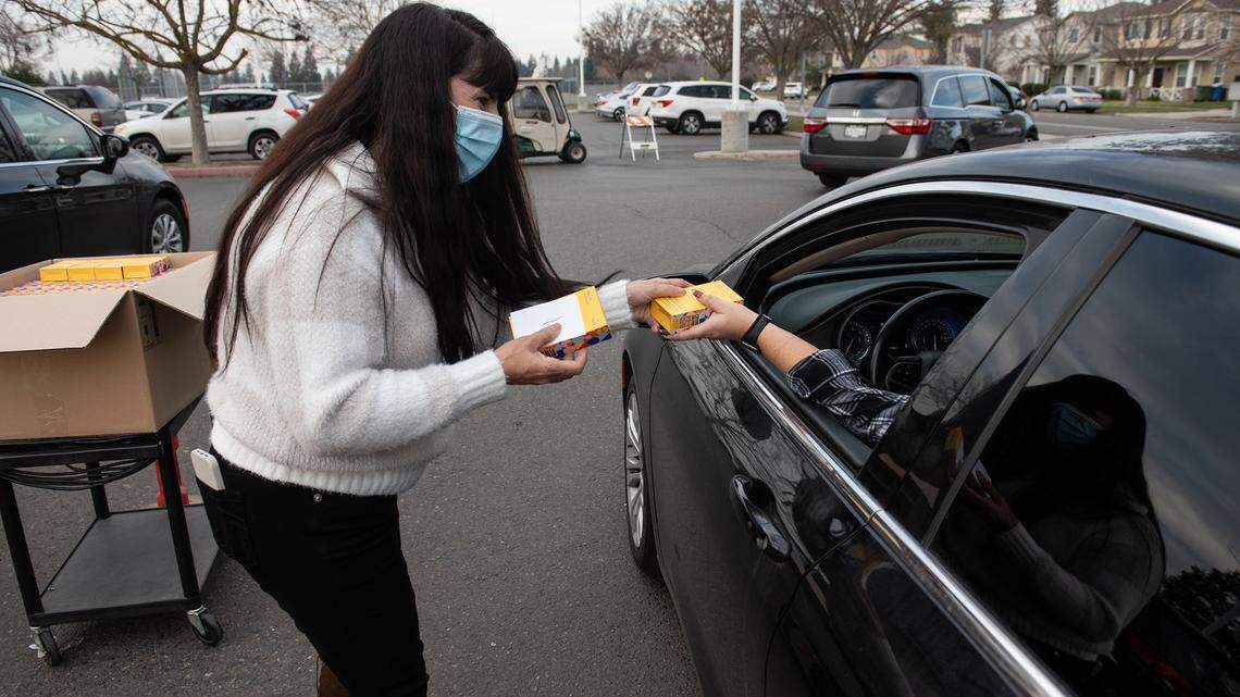 Pitman school employee Maria Johnson gives out COVID-19 rapid self test kits to students accompanied by a parent at Pitman High School in Turlock, Calif., on Thursday, Jan. 13, 2022.