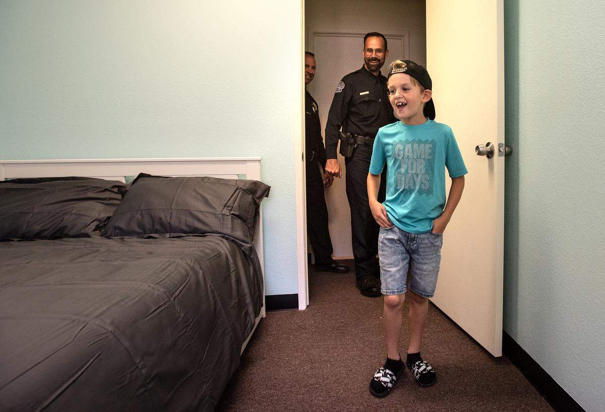 Landon Monk, 9, reacts to seeing his newly remodeled bedroom as Modesto Police detective Sean Dodge, watches in Modesto, Calif., on Friday, June 3, 2022. MPD and other local law enforcement members remodeled six rooms for nine children in Modesto and Empire through 10K with a Cop and the Healthy Room Project.