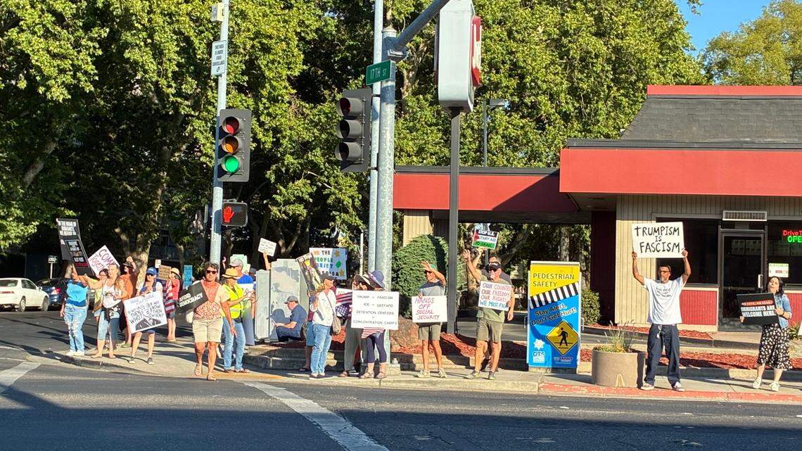 Dozens of people standing holding signs that read things like "Trumpism is Fascism" and "defend democracy" in front of a Jack in the Box in downtown Modesto. 