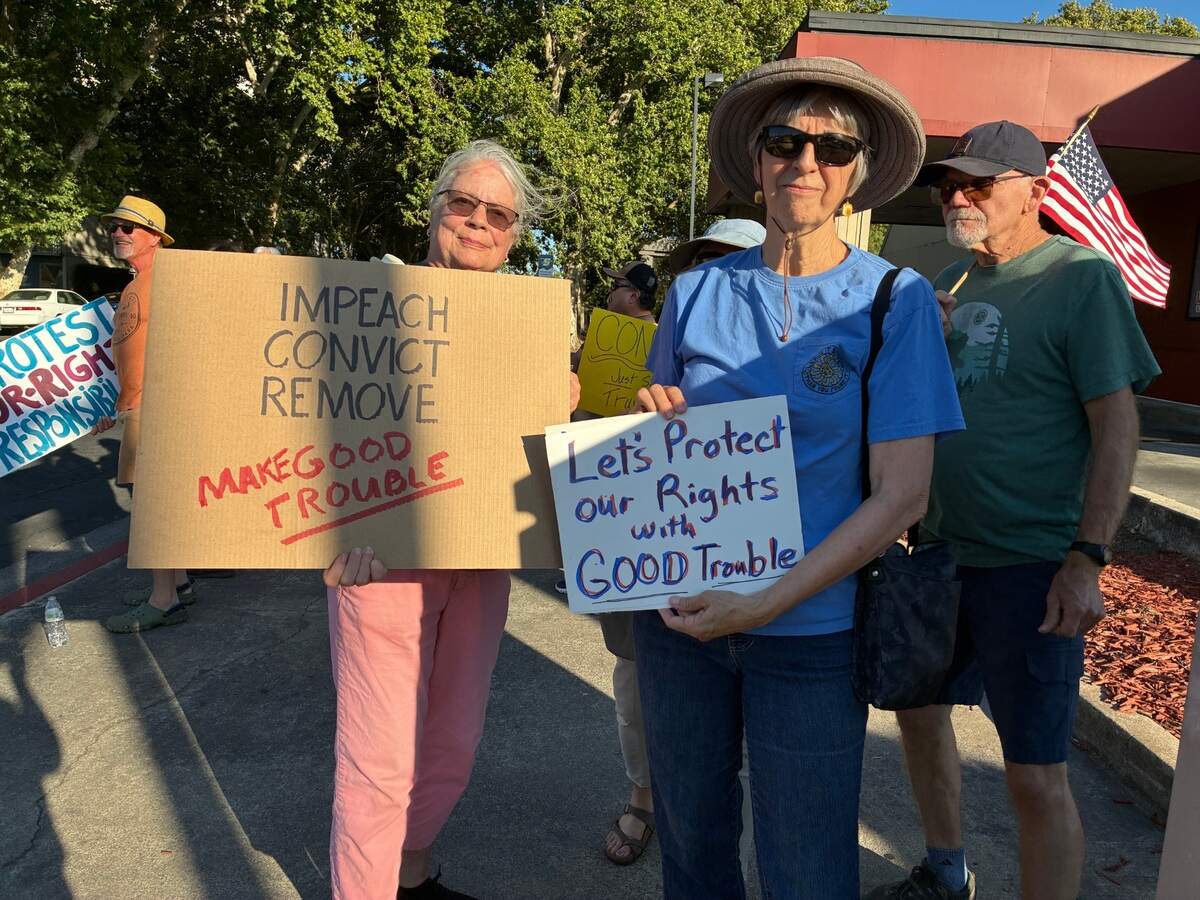 Two women smile and hold signs that read "Impeach. Convict. Remove. Make good trouble" and "Let's protect our rights with good trouble."