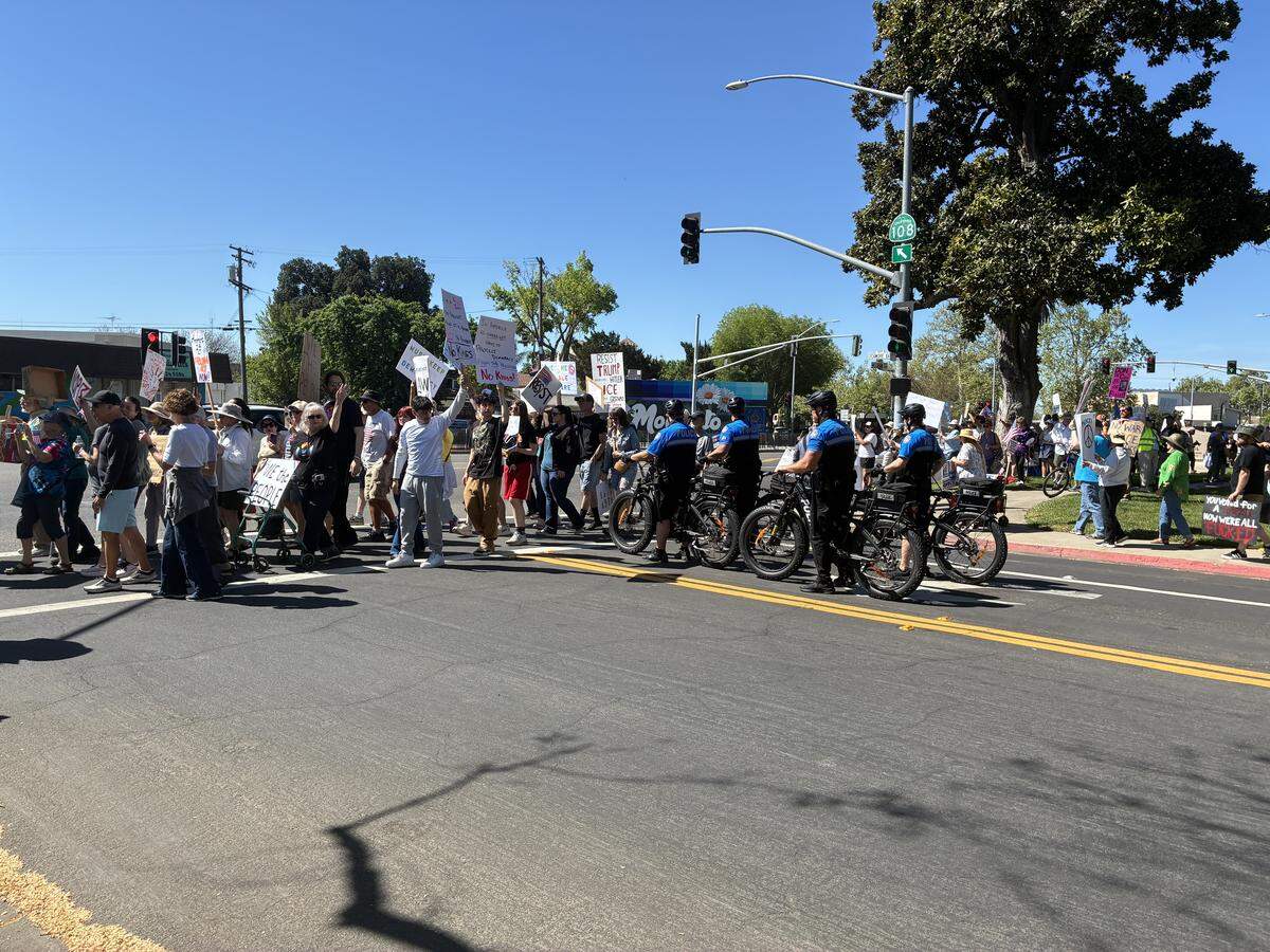 Modesto Police Department officers on bikes wait as protesters cross the street on their way to Five Points.