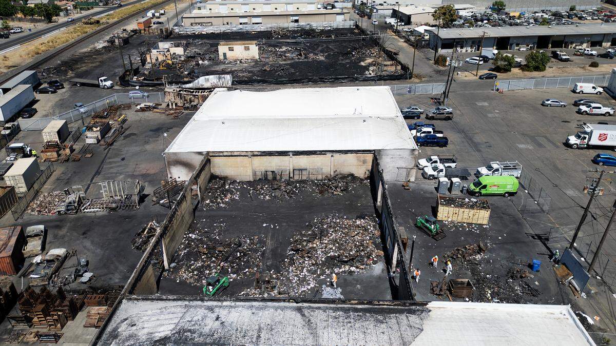 A crew clears the property of McGrath Moving and Storage which was destroyed by fire from an adjacent burning pallet business (above) on Aug. 9. Photographed in Modesto, Calif., Wednesday, Aug. 14, 2024.