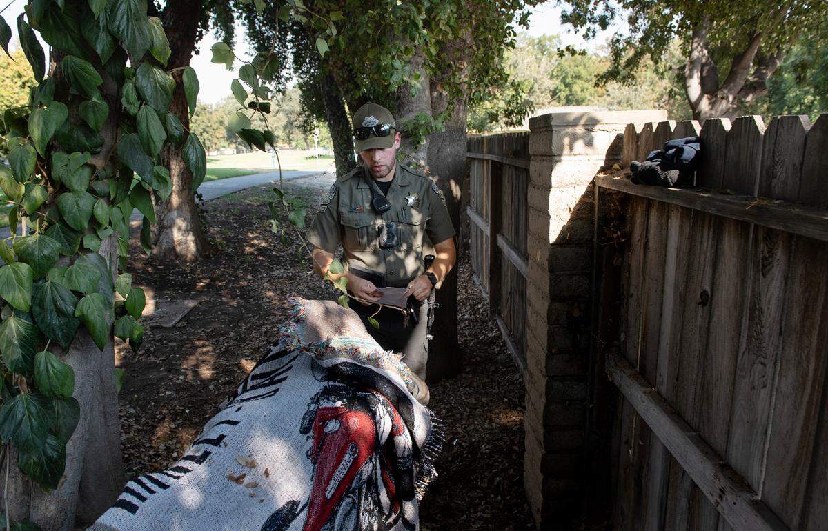 Modesto park ranger Justin Rocha places a 72-hour removal notice on a cart full of personal items at Downey Park in Modesto, Calif., on Friday, September 9, 2022.