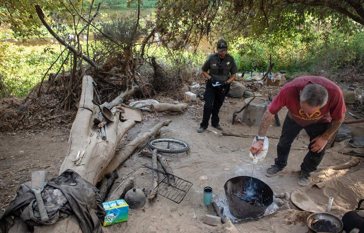 A homeless man puts out a cooking fire at the request of Modesto park ranger Justin Rocha in Modesto, Calif., on Friday, September 9, 2022.