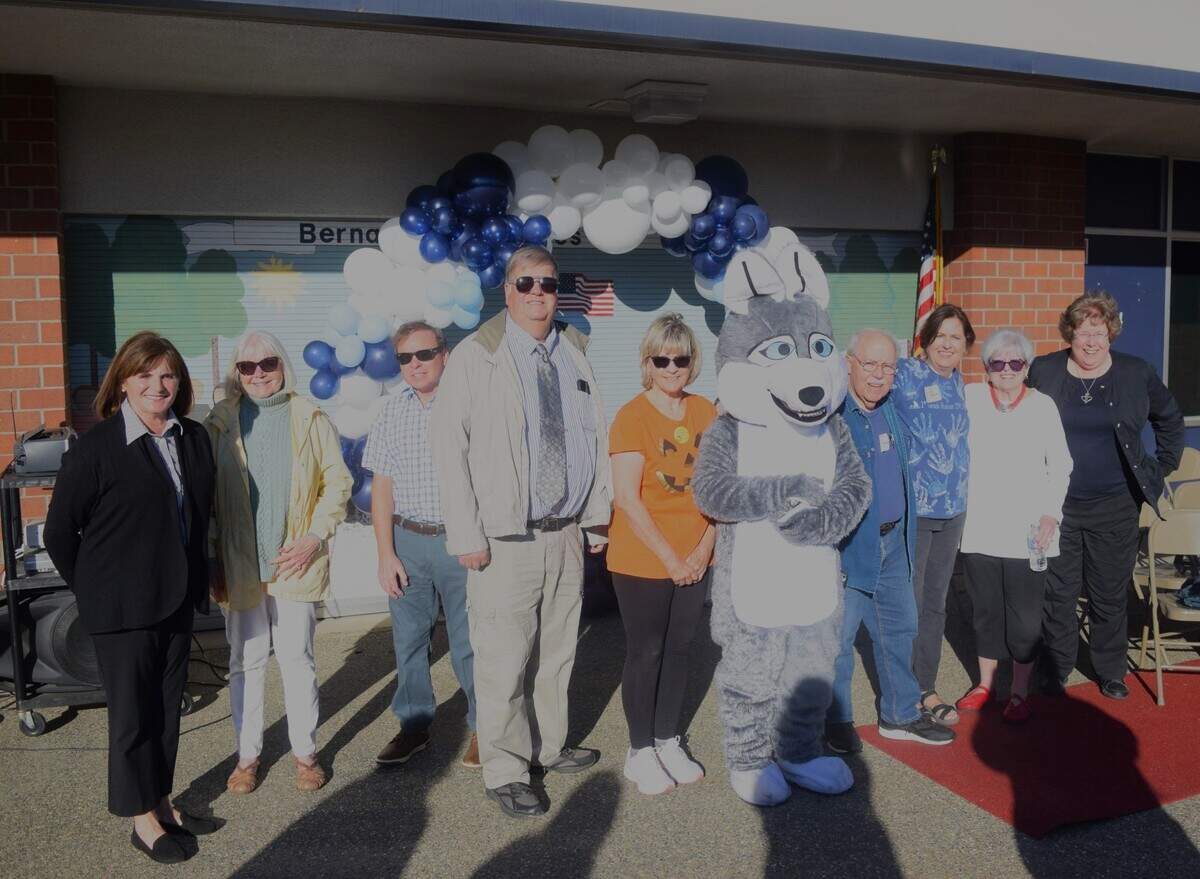 From left to right, Joanne Gaylor, Rosalie Reberg, Doug Bentley, Gordon Olsson, Candy Vargas, Gary McDaniel, Debbie Melton, Carole Davichi and Marilyn Glinskas pose with Snowball the Husky at the 35th anniversary of Bernard Hughes Elementary School on Oct. 18, 2024.
