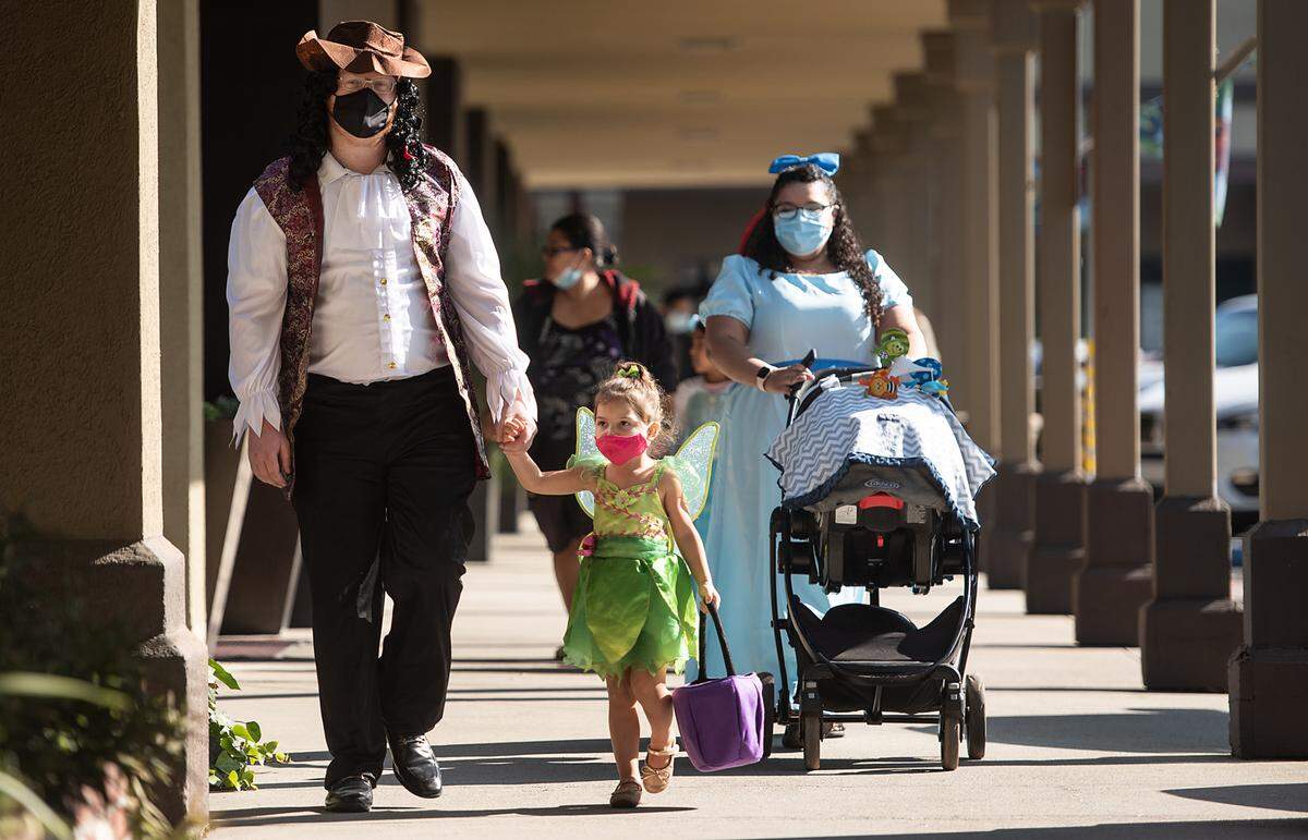 Andrew Dalen, left, holds his daughter Alina, 3, as his wife Jerika pushes their infant son as children and parents stop by shops for treats during “Trick Or Treat the Village” at McHenry Village in Modesto, Calif., on Saturday Oct. 31, 2020.