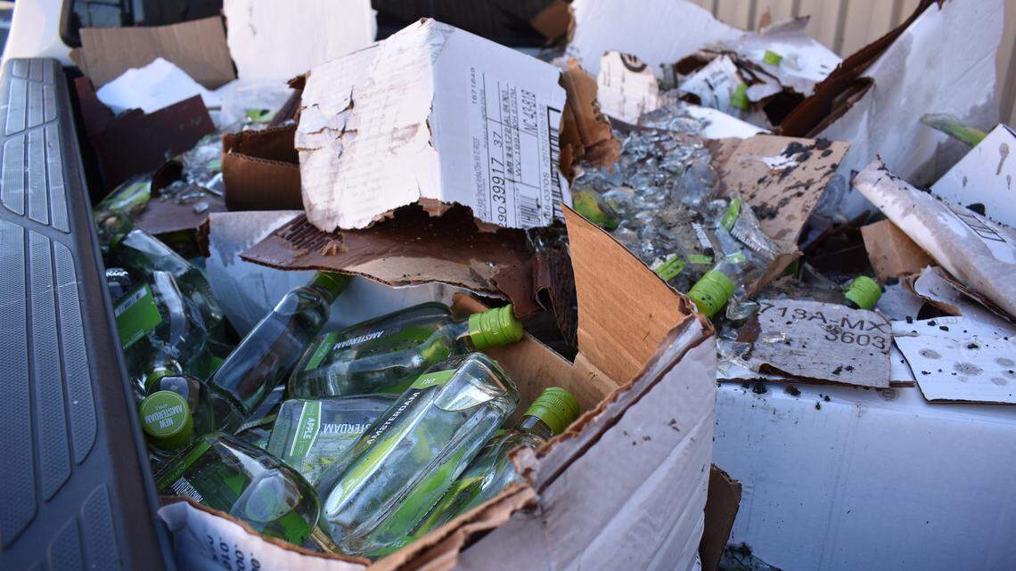 Broken and unbroken bottles of New Amsterdam Apple Flavored Vodka fill up pickup truck bed after a spill on the roadway.