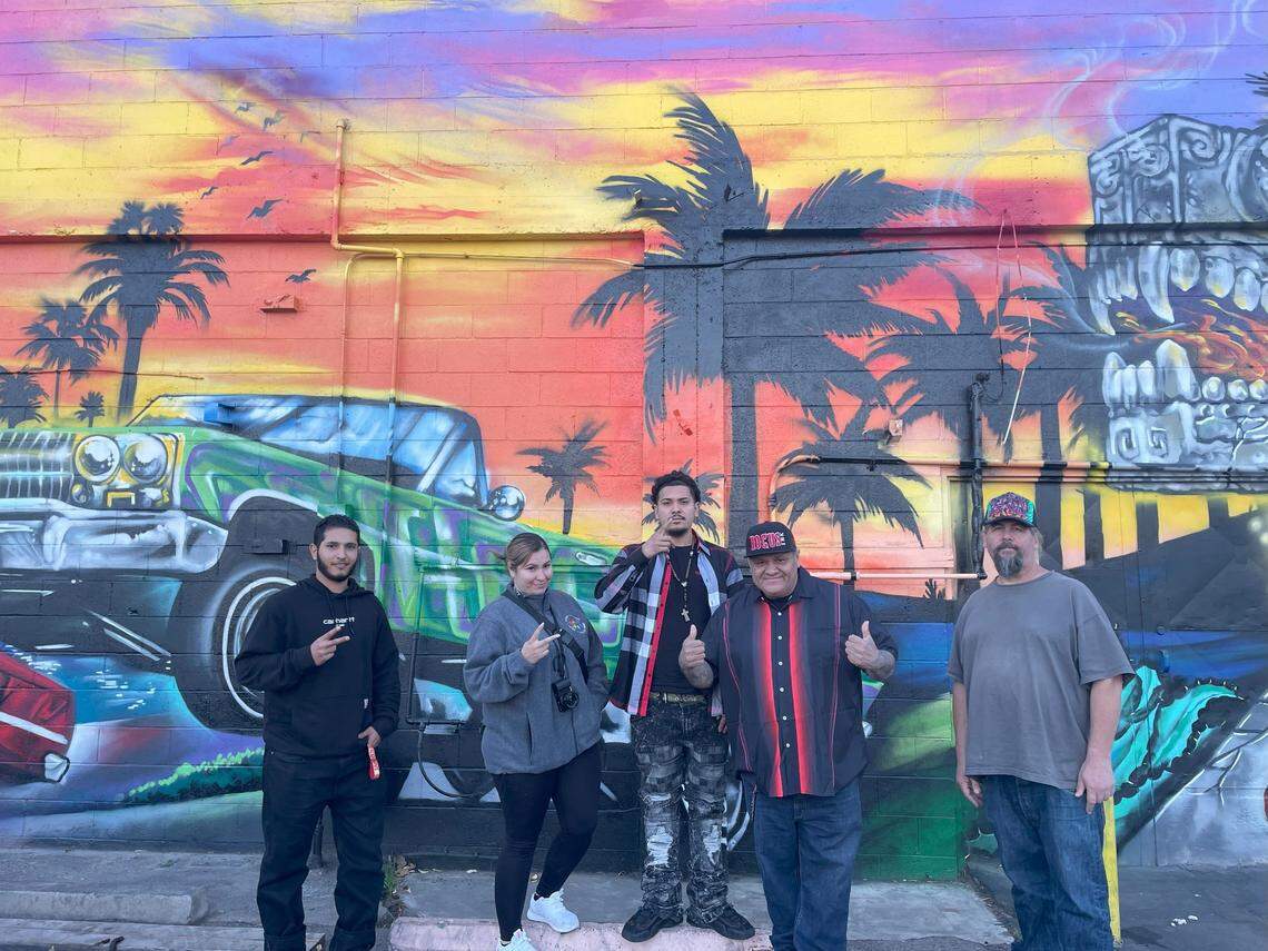 José 'Hocus' Manríquez (centro) con el gerente de Johnny's Market, Malek Shahibi; su hija Zsa Manríquez, su hijo Zayvian Manríquez y el pintor León Henry delante de su mural en H Street, en Modesto, California, el lunes 27 de noviembre de 2023.