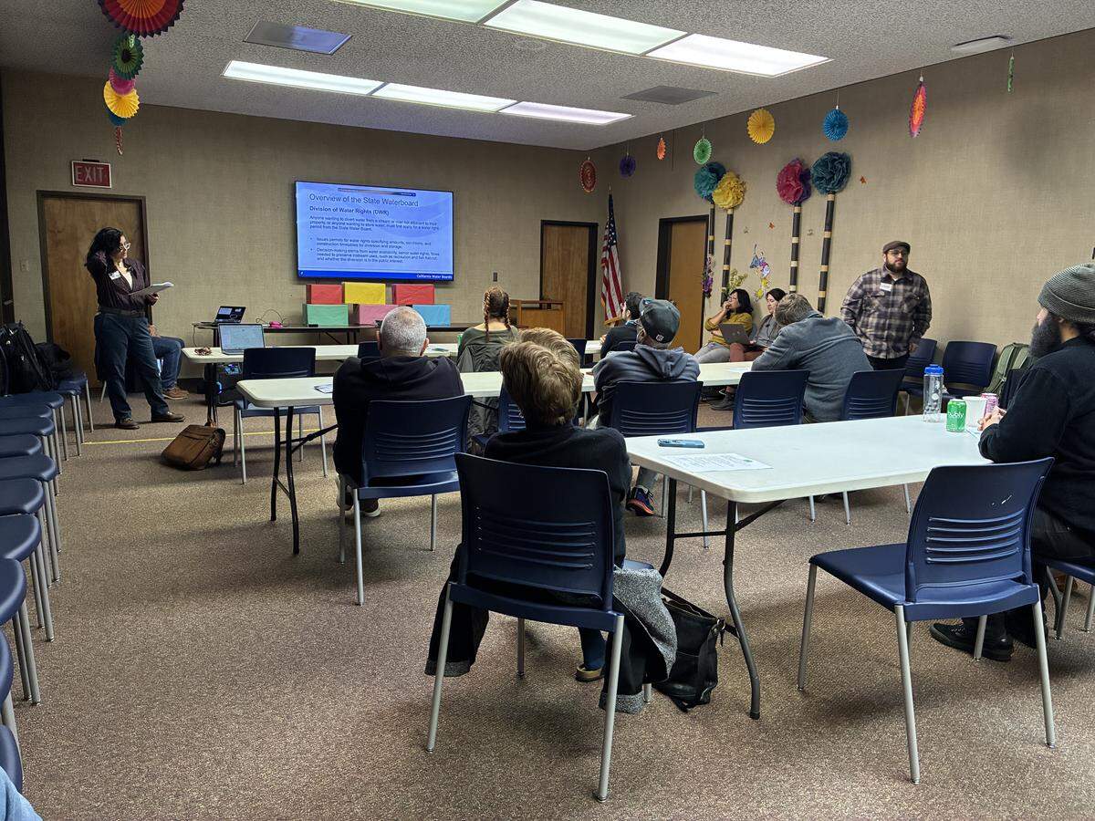 Residents sit in blue chairs at the Patterson Library community room facing a woman giving a powerpoint presentation.