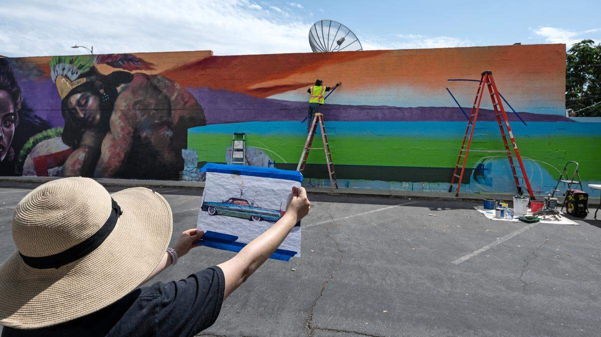 Perla Serna, a la izquierda, ayuda al artista Richard Gómez mientras se prepara para pintar un lowrider como parte del mural "Chicano Downtown", en Turlock, California, el sábado 9 de septiembre de 2023. Turlock West Side Story Mural Project se financia con una subvención de Heartland Creative Corps y el Carnegie Art Center.