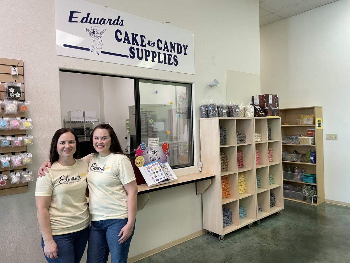 Sisters Emily Damante and April Brown, the co-owners and operators of Edwards Cake and Candy Supplies, under the original store sign from when their grandmother started the business in 1977.