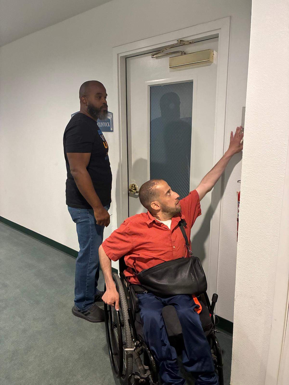 A man in a wheelchair reaches high to ring a doorbell on a closed office.