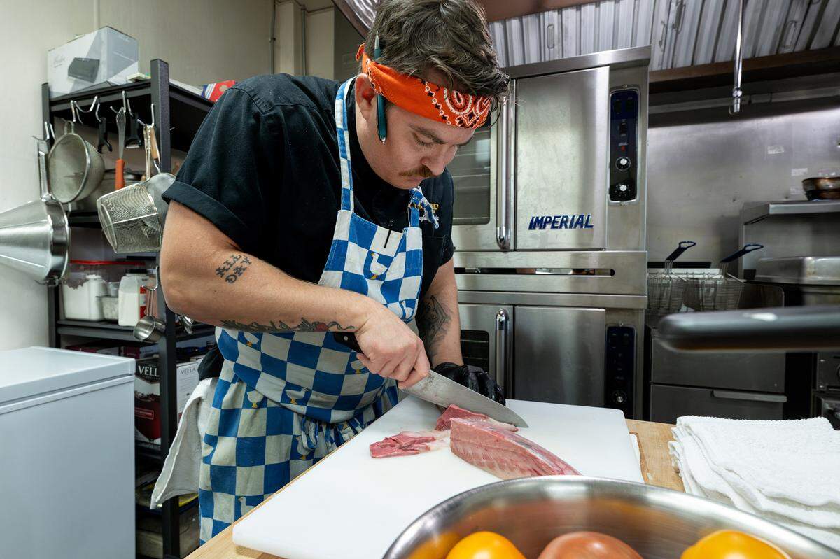 Chef Nathan Heese slices yellowtail for a sashimi dish at Lo-Fi Laboratories artisan cocktail lounge in Modesto, Calif., Wednesday, Aug. 23, 2023.