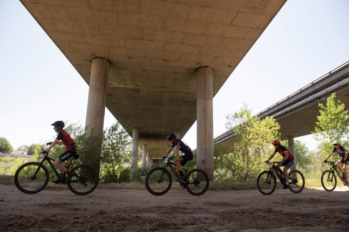 Riders from the boys junior varsity division II pass under the Highway 99 bridge in the Tuolumne River Regional Park during the NorCal Interscholastic Cycling League event in Modesto, Calif., on Saturday, April 9, 2022.