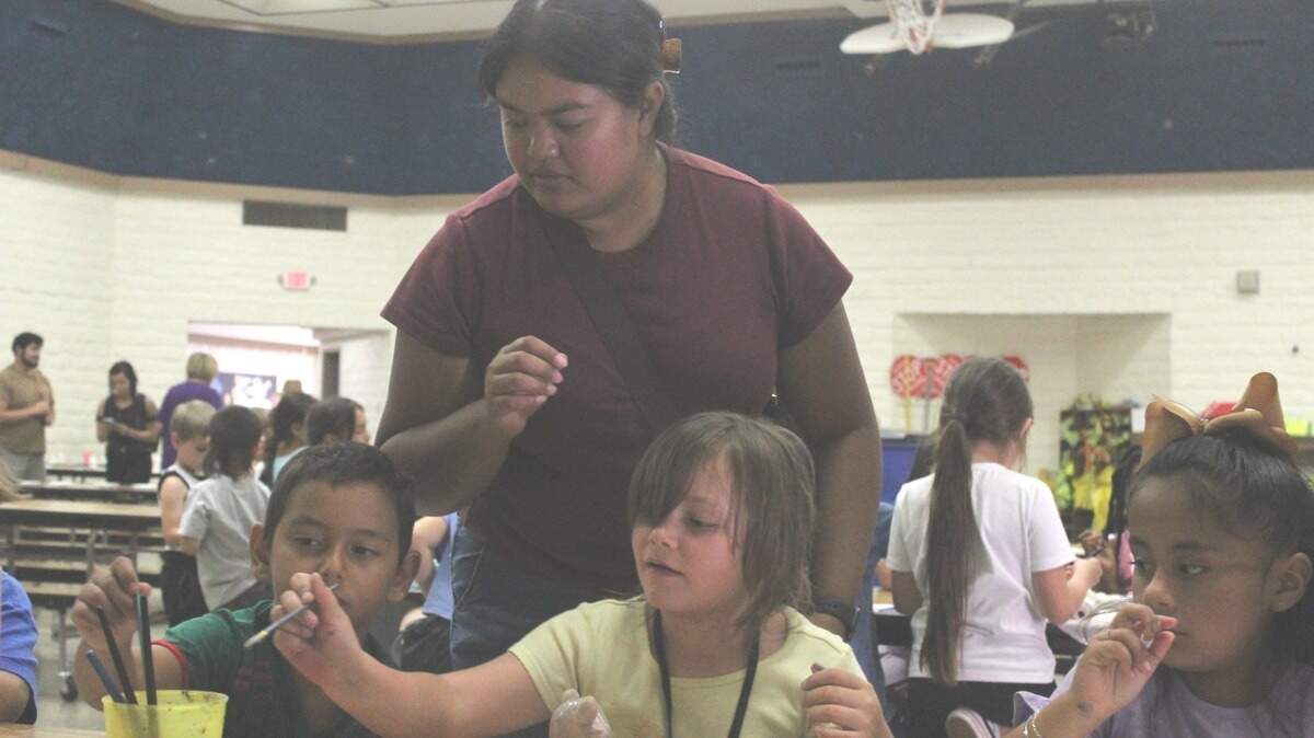Brianna Kem, an afterschool paraprofessional, assist students in painting their ceramic clay animals.