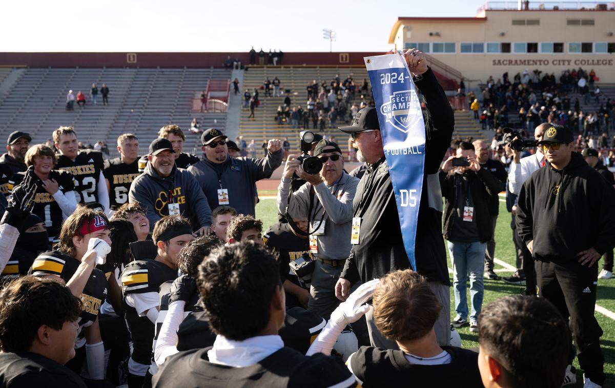 Hughson coach Shawn King holds up the section banner as he talks with team after the Huskies 30-29 victory over Sutter in the Sac-Joaquin Section Division 5 championship game at Sacramento City College in Sacramento, Saturday, Nov. 30, 2024.