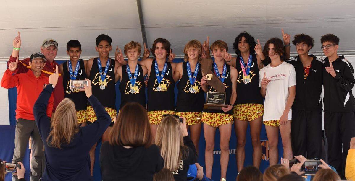 Oakdale cross country runner pose with head coach Guy Fowler and assistant coach Vic Moreno after winning the Division III State Championship at Woodward Park in Fresno on Saturday, Nov. 26, 2022.